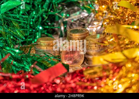 Pila di monete con un euro davanti e con decorazioni natalizie intorno Foto Stock