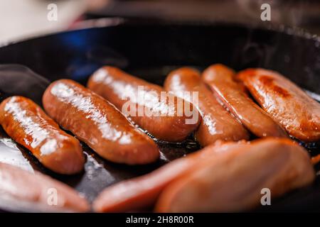 le salsicce tagliate a metà vengono fritte in olio in una padella in ghisa nera - primo piano con fuoco selettivo Foto Stock