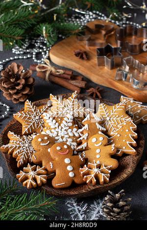 Biscotti fatti in casa di pan di zenzero sotto forma di favolosi uomini di pan di zenzero, fiocchi di neve e alberi di natale su piatto di legno in composizione anno nuovo così come Foto Stock