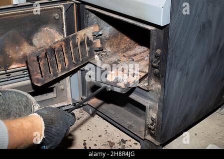 Pulizia della caldaia a combustibile solido dai resti di legna e carbone. Caldaia con smorzatore aperto. Efficienza di riscaldamento in casa. Foto Stock