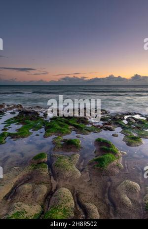 tramonto sulle rocce su un'isola di wight beach, isola della costa di wight sotto la luce atmosferica, isola di wight shoreline, rocce ricoperte di alghe. Foto Stock