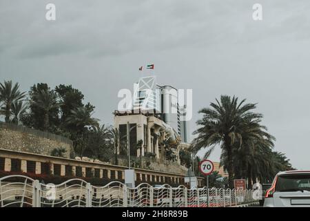 Traffico di auto su strada Jumeirah di Dubai con pedane stradali, palme, semafori e oggetti turistici Foto Stock