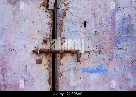 Sfondo e primo piano di una vecchia porta in metallo resistente alle intemperie fissata con un dispositivo di chiusura in metallo Foto Stock