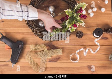 Donna artigiana che fa Natale festa wreath su un tavolo tra da arredamento di Capodanno Foto Stock