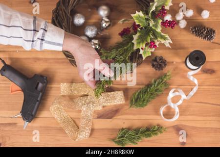 Donna artigiana che fa Natale festa wreath su un tavolo tra da arredamento di Capodanno Foto Stock