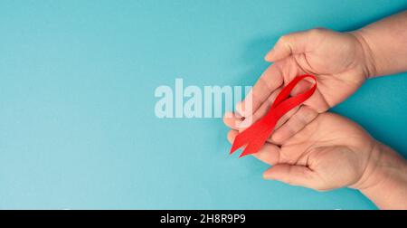 Mani con nastro rosso per la consapevolezza dell'AIDS, sfondo blu con spazio di copia per il testo Foto Stock