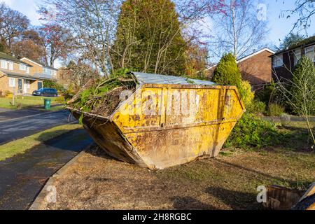 Un grande arrugginito, rifiuti di rifiuti martoriati saltare pieno di rami e rifiuti di giardino sul giardino di fronte di una strada a Surrey, nel sud-est dell'Inghilterra Foto Stock