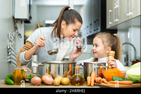 Madre emozionale e piccola figlia degustazione zuppa insieme Foto Stock