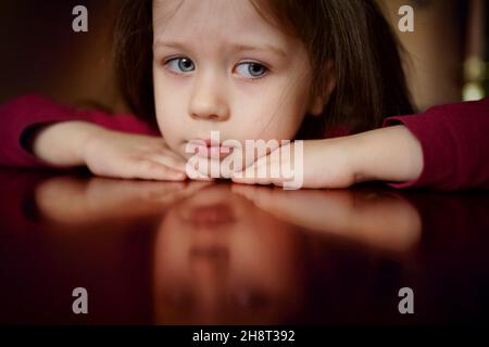 Triste testa di una bambina si trova sul tavolo, pensa, sconvolto, offeso, riflessione del volto Foto Stock