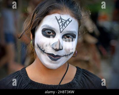 Giovane messicana con il tradizionale viso di Catrina bianca e occhi neri sul giorno dei morti (Día de los Muertos) guarda lo spettatore. Foto Stock