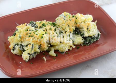 Contorno di patate e spinaci con panko grattato e parmigiano sul piatto da portata rosso Foto Stock