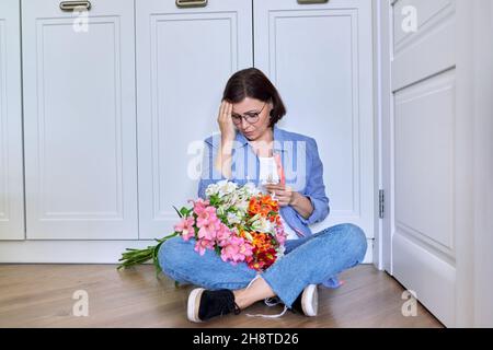 Triste turbata donna di mezza età con un bouquet di fiori Foto Stock