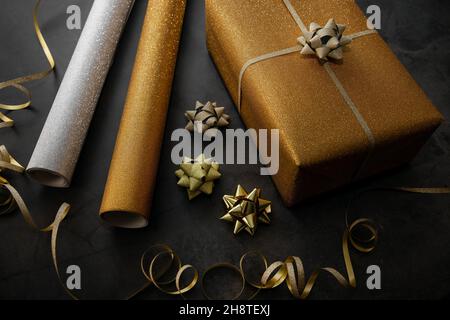 confezione regalo. regalo dorato avvolto con rotoli di carta da imballaggio e accessori su sfondo di pietra nera Foto Stock