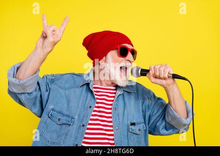 Ritratto di attraente allegro funky talento uomo grigio-capelli canti colpo rock roll mostrando corno isolato su sfondo di colore giallo lucido Foto Stock