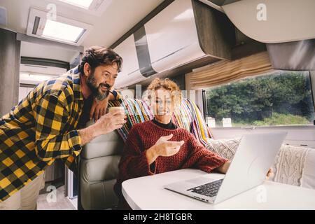 La coppia adulta si diverte a lavorare insieme utilizzando un computer portatile all'interno di un camper. Concetto di nomade e stile di vita libero alternativo del lavoro. M moderno Foto Stock