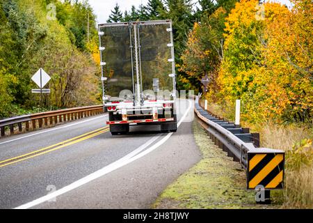 Semirimorchio industriale a carro grande per il trasporto di carichi commerciali in semirimorchio con portellone in metallo a specchio che corre sulla tortuosa strada autunnale Foto Stock