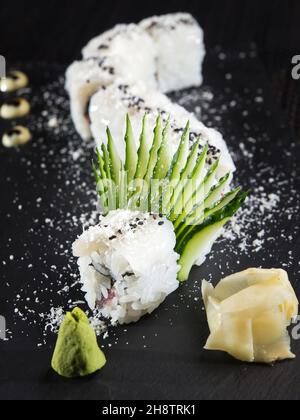 rotolo di sushi con sesamo su un piatto di pietra nera, foto ravvicinata su sfondo scuro Foto Stock