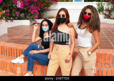 Tre amici latini in posa per la macchina fotografica nel parco con maschera protettiva Foto Stock