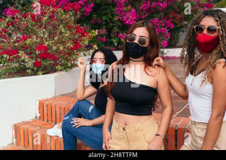 Tre amici in posa per la macchina fotografica nel parco con maschera protettiva Foto Stock