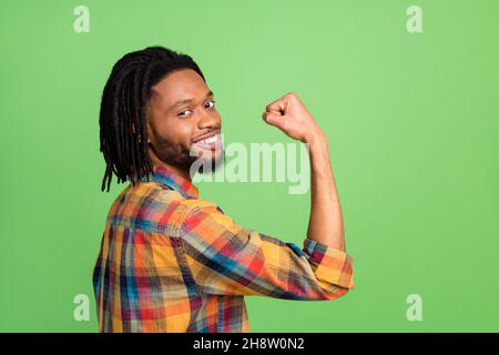 Foto di divertente forte pelle scura uomo indossare camicia a quadri sorridente crescente pugno isolato sfondo verde di colore Foto Stock