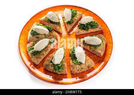 Quenelle di merluzzo veneziano cremato con spinaci su fette di focaccia integrale, su piatto arancione isolato su bianco Foto Stock