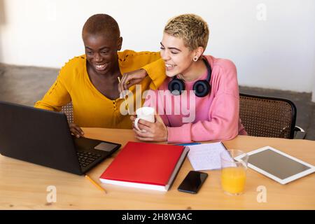 Femmine sorridenti multietniche che usano un computer portatile in ufficio Foto Stock