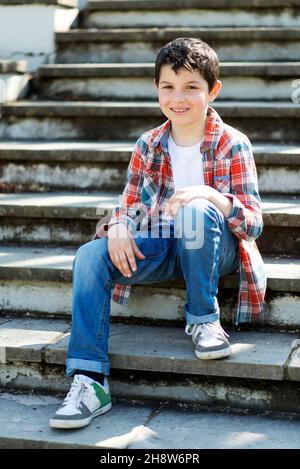 Ragazzo allegro seduto su bleachers al parco della città mentre si guarda la macchina fotografica Foto Stock