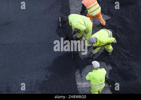 I lavoratori durante l'asfaltatura della strada lavorano sulla strada della città. Pavimentazione in asfalto. Vista ad angolo alto. Spazio di copia Foto Stock