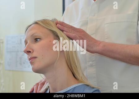 Un chiropratico maschile regola la testa, il collo e la colonna vertebrale di una paziente femminile. Inghilterra, Regno Unito Foto Stock