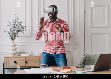 L'uomo africano in visore VR interagisce con l'interfaccia digitale, utilizzando un dispositivo innovativo per le aziende Foto Stock