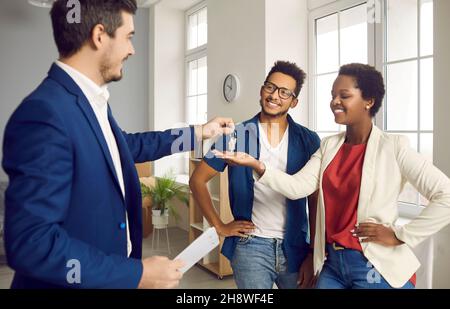 Agente immobiliare o immobiliare dà le chiavi a casa nuova per felice giovane coppia nera Foto Stock