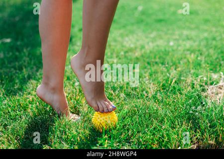 gomma da massaggio spiky per il rilascio miofasciale e il miglioramento del sistema linfatico, piedi donna su erba verde in foresta Foto Stock