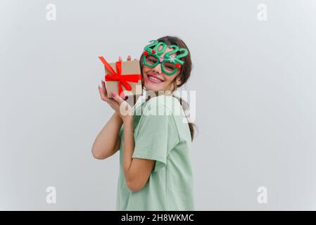 Foto di una giovane donna felice stupito con un sorriso tenere una mano un regalo di Natale isolato su uno sfondo bianco. Foto Stock