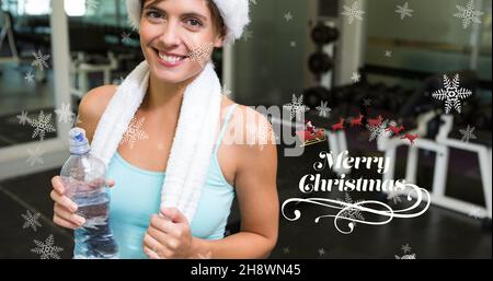 Composizione del saluto di natale con sorridente giovane caucasica che tiene bottiglia d'acqua in palestra Foto Stock