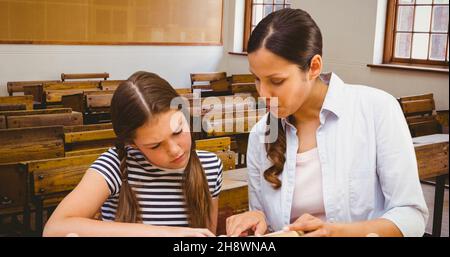 Giovane insegnante che guida la scolgirl mentre insegna e spiega in aula a scuola Foto Stock