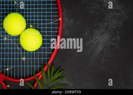 Tennis. Composizione sportiva con palline da tennis gialle su racchetta con foglia di palma su sfondo nero con spazio di riproduzione. Sport e stile di vita sano. Il Foto Stock