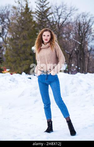 Ritratto di una giovane bella donna bionda in maglia beige in posa nel parco invernale Foto Stock