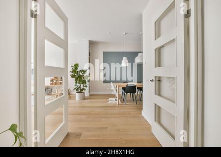 Corridoio con pareti bianche vicino alla sala riunioni arredato con sedie e tavolo posto su pavimento in legno sotto lampade pendenti Foto Stock