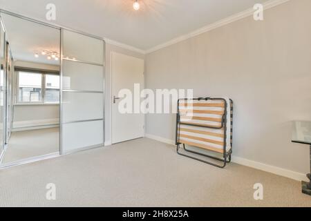 Accampamento in metallo ripiegato posto a parete bianca in camera spaziosa vuota con armadio vicino porta chiusa in appartamento moderno Foto Stock