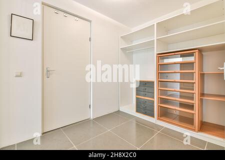 armadio aperto con ripiani vuoti e cassetti posti a parete in camera spaziosa e luminosa con porta bianca chiusa in appartamento Foto Stock