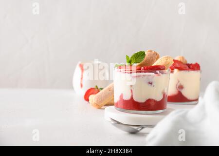 Trifle di fragole a strati in vasetti di vetro con biscotti savoyardi, mascarpone e biscotti con panna montata. Primo piano. Tiramisù italiano con frutti di bosco Foto Stock