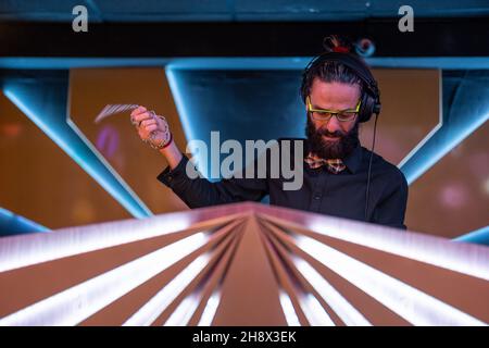 DJ maschile concentrato giovane bearded in occhiali e cuffie in piedi al banco illuminato nel moderno nightclub Foto Stock