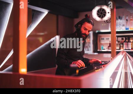 DJ maschile concentrato in cuffia in piedi al banco illuminato nel moderno nightclub Foto Stock