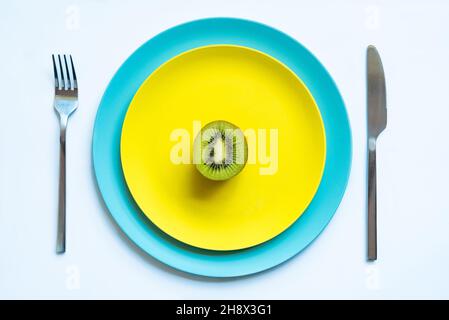 Da sopra di metà di kiwi succosa freschi maturi posti su piatti gialli e blu su superficie bianca Foto Stock