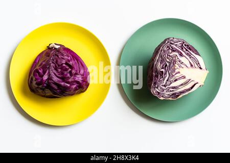 Da sopra di cavolo rosso dimezzato messo su piatti gialli e verdi su sfondo bianco Foto Stock