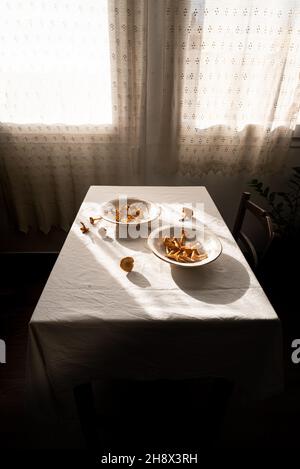 Angolo alto di funghi raccolti in foresta in ciotole poste sul tavolo vicino finestre in casa villaggio Foto Stock