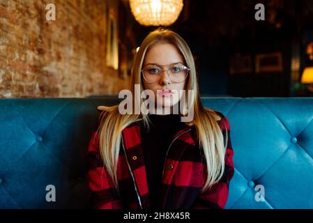 Fiducioso bella giovane donna bionda seduto su un bar e guardando la macchina fotografica Foto Stock