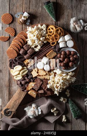 Vista dall'alto di vari cioccolatini con biscotti e popcorn disposti su un tavolo di legno con figure di natale Foto Stock