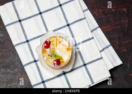 Torta con gelatina, kiwi, ciliegie e mango sul tavolo. Mini dessert yummy su sfondo di legno, primo piano. Foto Stock