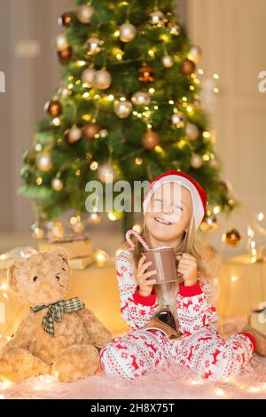 Bella ragazza caucasica di cinque anni che indossa pigiama di Natale quando si diverte a casa durante le vacanze invernali. Buon Natale e felice anno nuovo Foto Stock